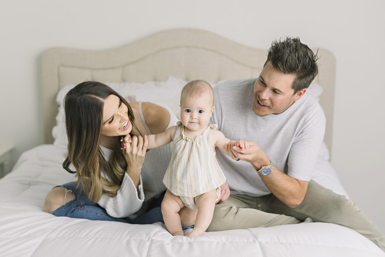 Parents helping baby stand on bed during in-home family session, Boise baby photos
