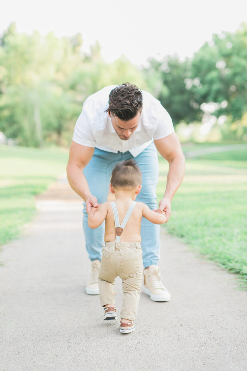Dad helping toddler walk down sunny park path, Boise family photographer