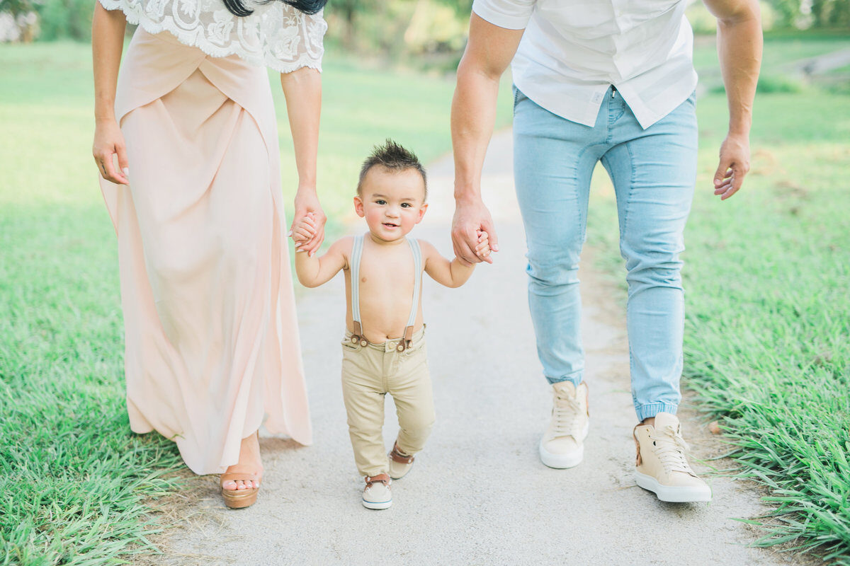 Family of three walking hand in hand down park path, outdoor family photography