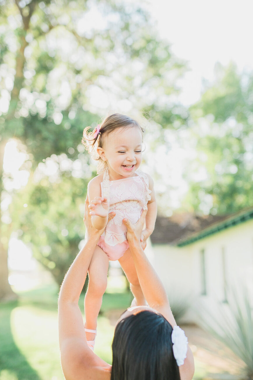 Mother lifting laughing toddler into the air, candid family photography session