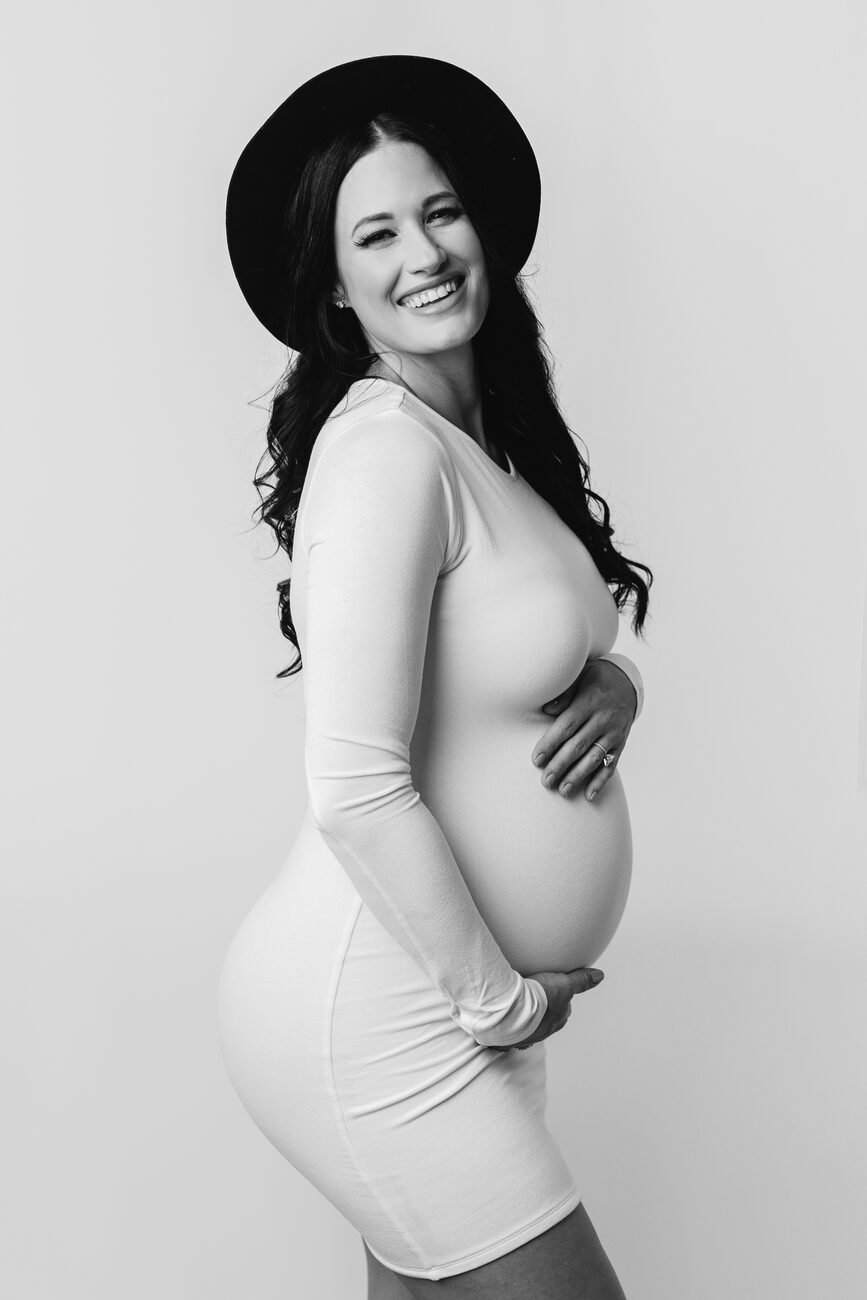 Smiling expecting mother in white dress and brimmed hat, editorial Boise maternity portrait
