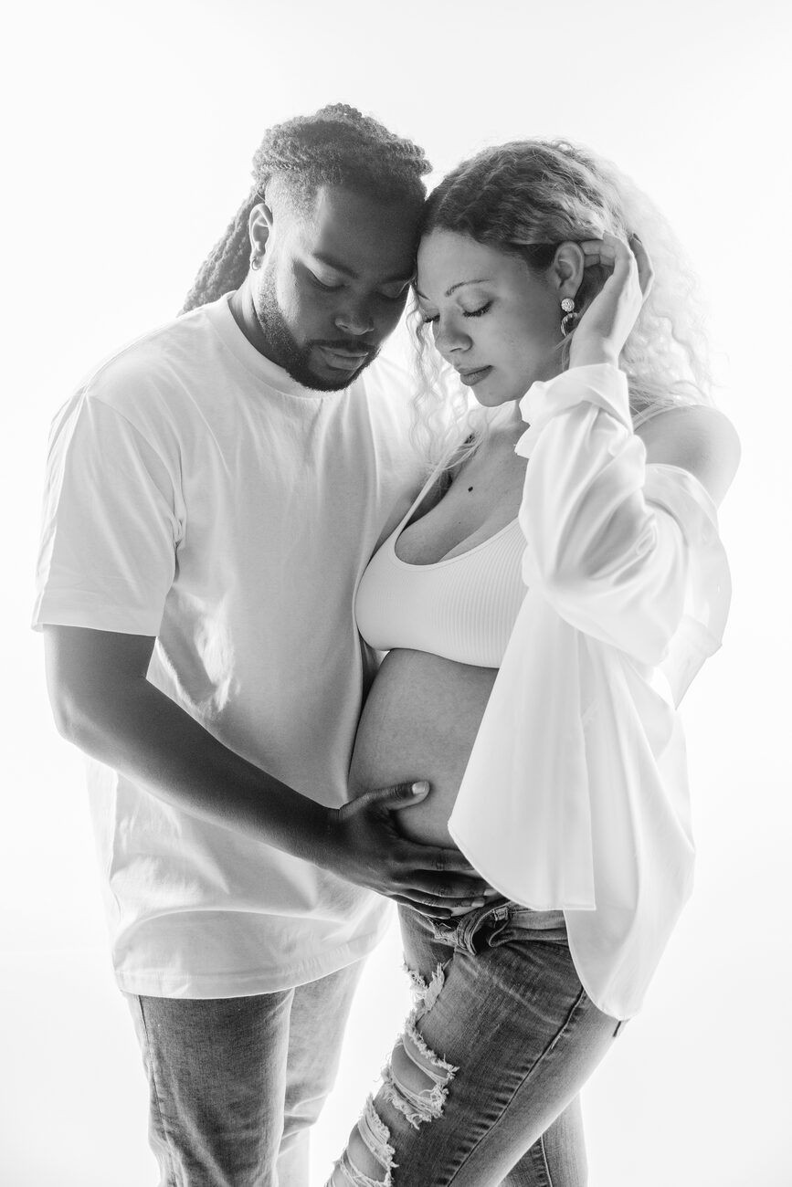 Boise maternity photography session, couple embracing with hands on belly in bright studio light