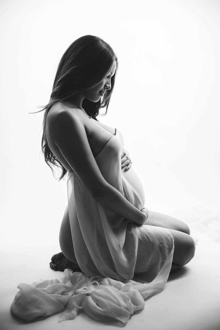 Expecting mother kneeling in flowing sheer fabric, fine art Boise maternity photos in studio