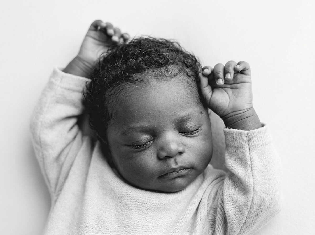 Sleeping newborn with curly hair and arms raised, black and white portrait by a Boise newborn photographer