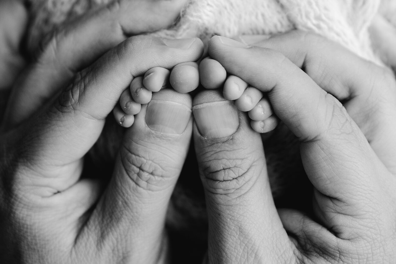 Parents’ hands wrapped around their newborn’s tiny toes, black and white macro in Boise, Idaho
